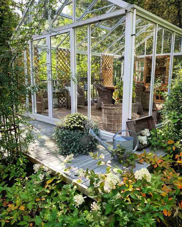 حديقة شتوية باردة مصنوعة من الزجاج مع كراسي بذراعين من القش ومساعدات التسلق لتسلق النباتات