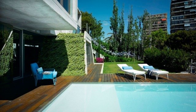 الفناء الخلفي مع حمام السباحة سطح خشبي مع كراسي الاستلقاء للتشمس والجدار الأخضر
