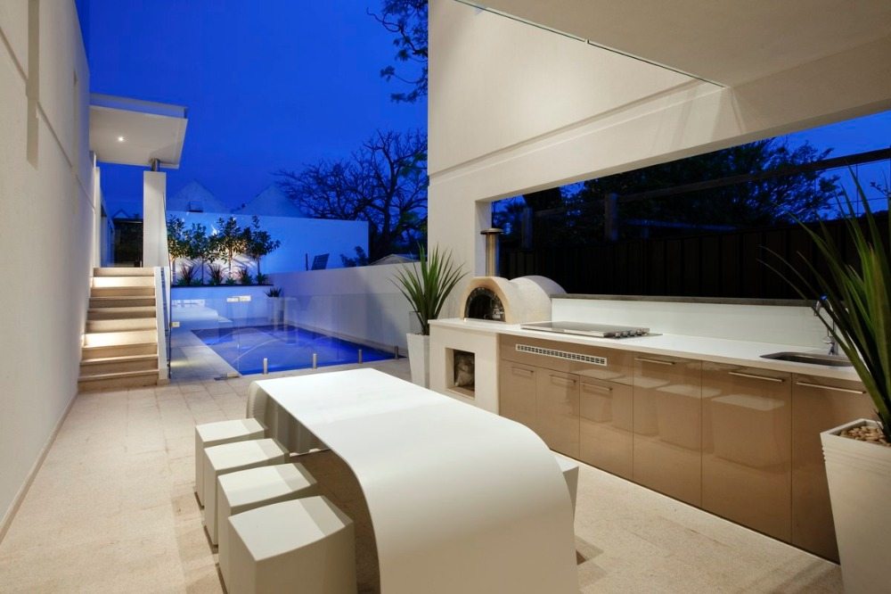 أثاث مطبخ فاخر باللون البيج مع فرن بيتزا وطاولة مصممة باللون الأبيض بجوار حمام السباحة