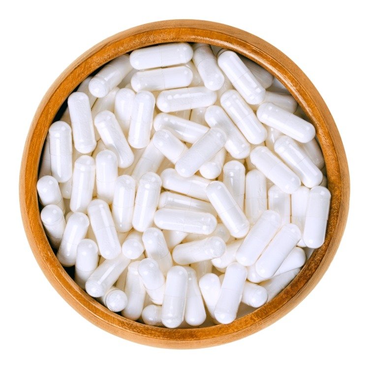 كبسولات بيضاء كمكمل لفيتامين ب المركب في وعاء خشبي