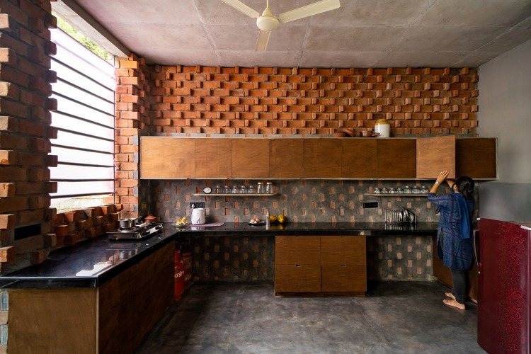 تستخدم ربة المنزل الخزائن الخشبية في المطبخ مع جدار من الطوب بالداخل وتكسية الجدران الخرسانية