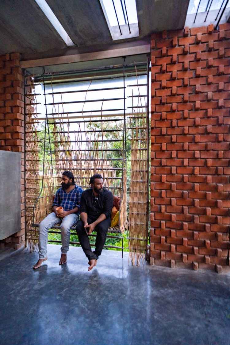 يجلس مهندسان معماريان من مكتب Wallmakers للهندسة المعمارية على أرجوحة في المنزل الذي تم تشييده مؤخرًا مع وجود جدار من الطوب بداخله