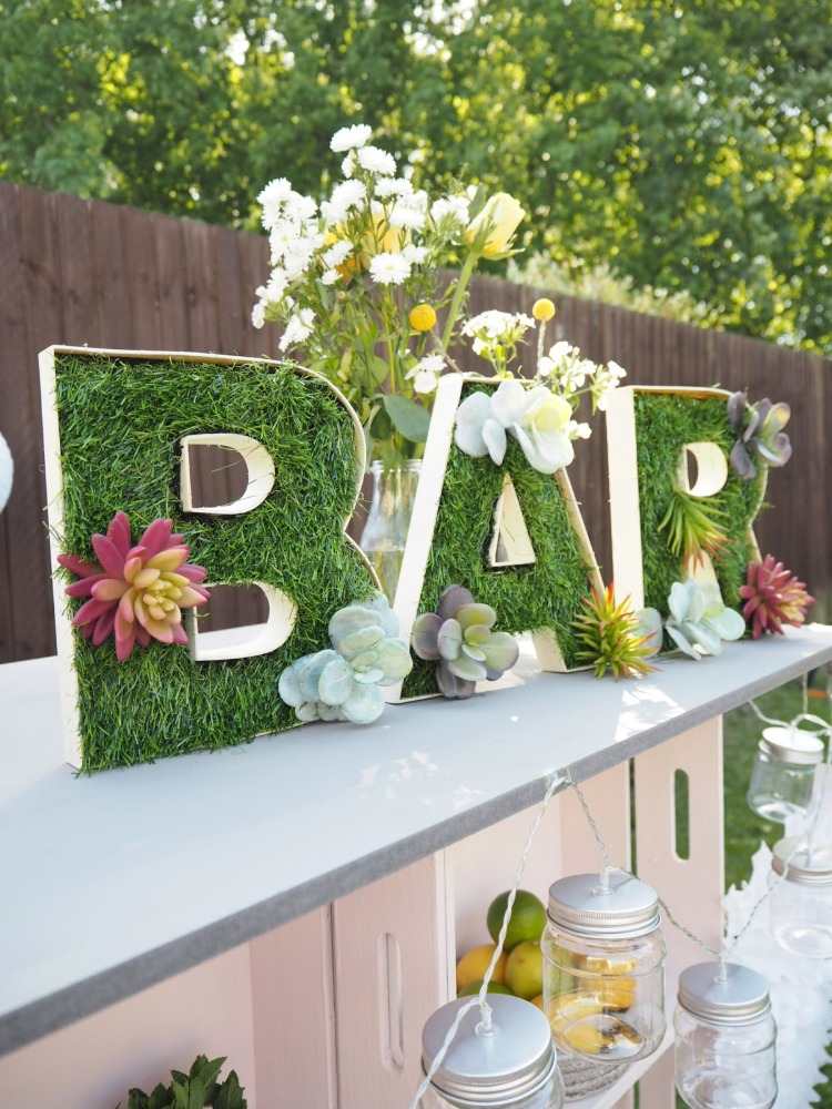 تركيبة ملونة كديكور لطاولة البار في الحديقة تتكون من أكواب بلاستيكية زهرية وأزهار على حروف مع عشب صناعي