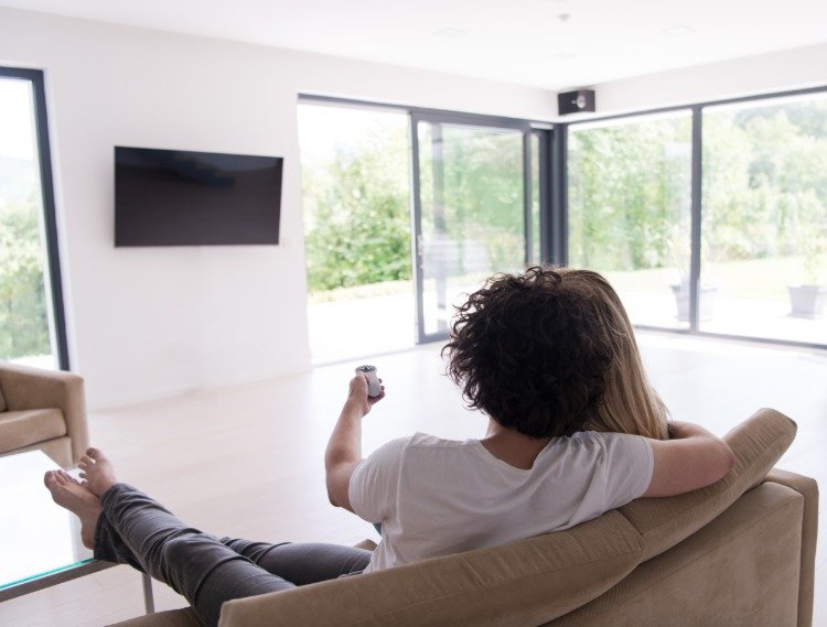 زوجان يجلسان على الأريكة ويقومان بتشغيل تلفزيون بشاشة مسطحة على الحائط