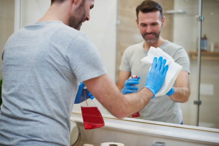 رجل مبتسم مع قفازات مطاطية تنظيف خزانة الحمام بواجهة مرآة