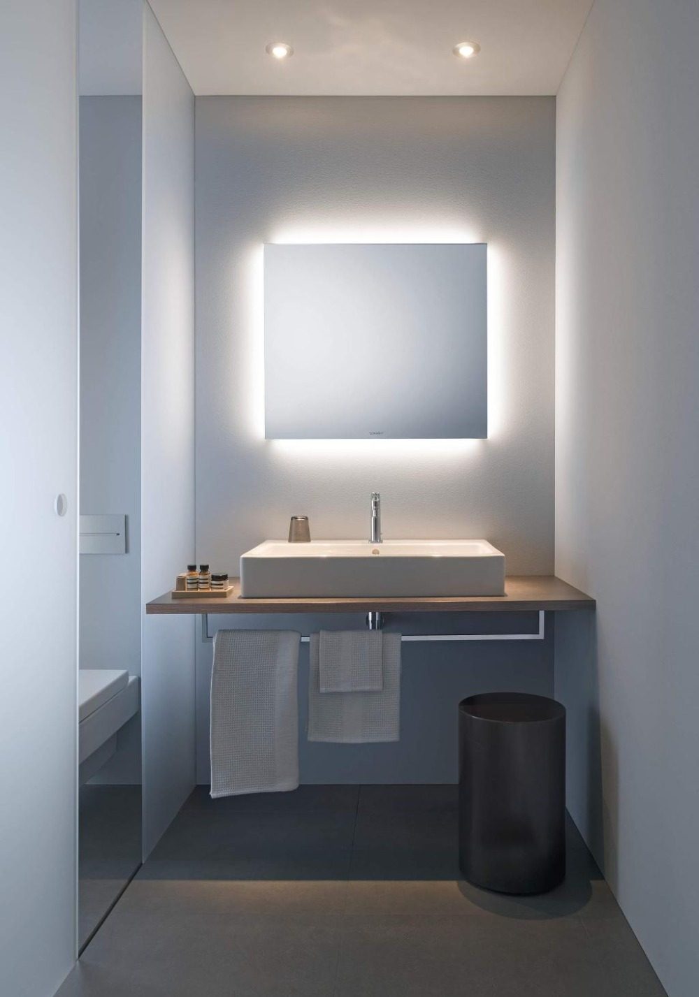 حمام ضيق مع مغسلة ومرآة مربعة ، مضاء بشكل غير مباشر