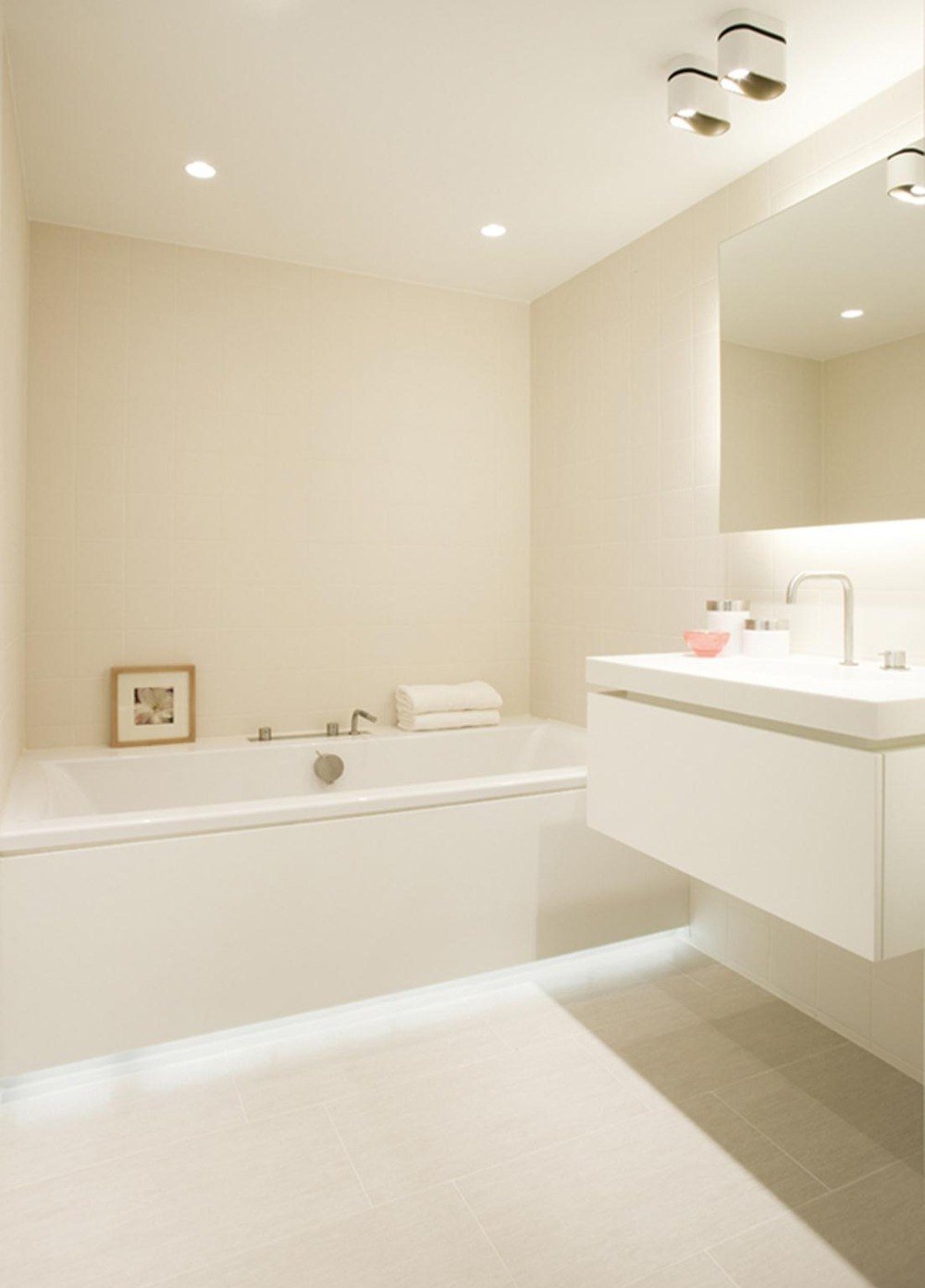 حمام ذو إضاءة غير مباشرة باللون الأبيض مع حوض استحمام وإضاءة مرايا سرية