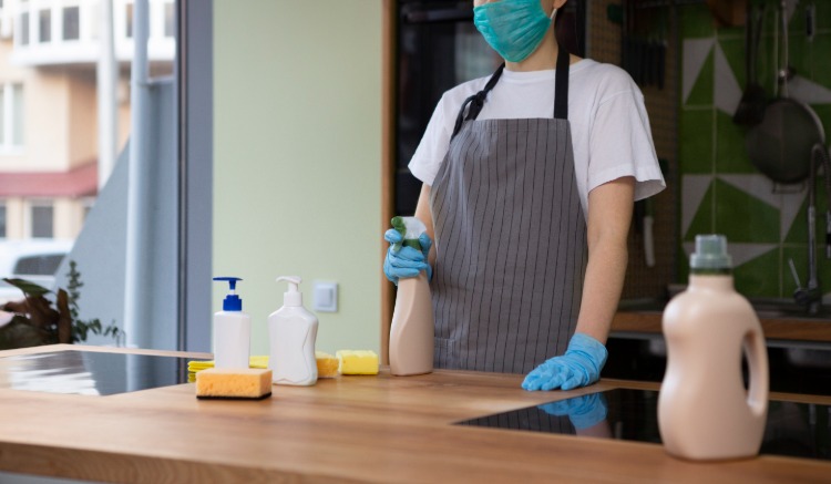 امرأة مع قناع واقي تنظيف سطح عمل المطبخ الخشبي مع المنظفات
