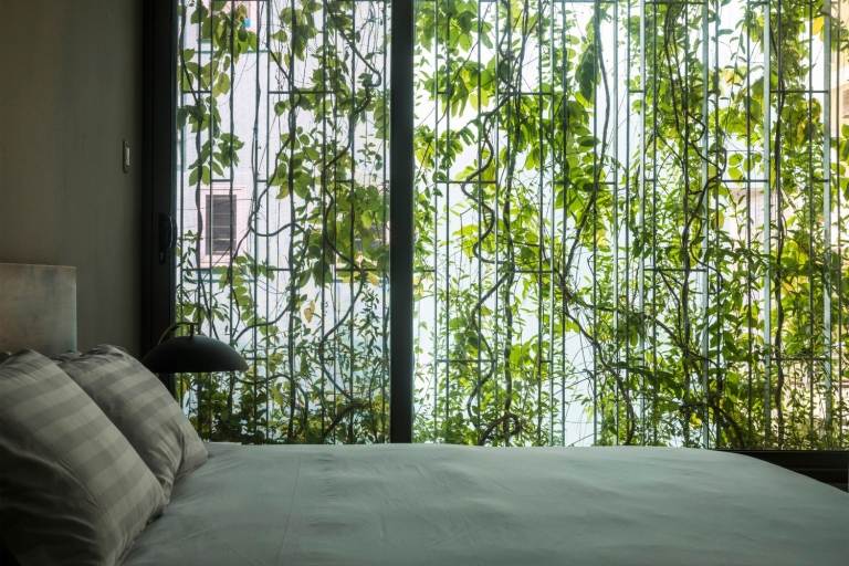 غرفة نوم مع سرير مزدوج وإطلالة على واجهة المنزل مع النباتات تحت المظلة