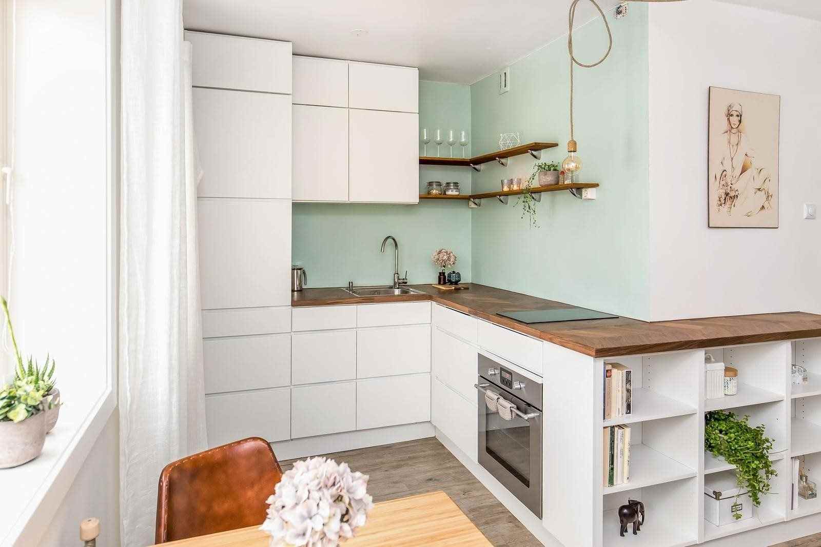 تستخدم زوايا المطبخ سطح عمل خشبي واجهات بيضاء بدون مقبض بلون أخضر فاتح للجدار